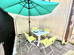 Een terras met een tafel, stoelen en een parasol, en een muur met structuur.