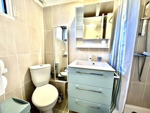 Een kleine badkamer met toilet, wastafel, spiegel en douche.