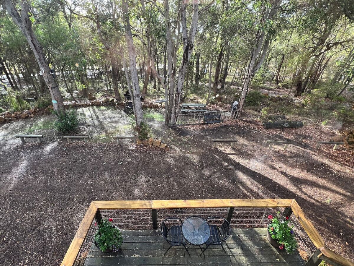 A forested area with picnic tables and a small seating area with a table and chairs.