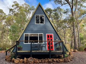 A small, dark blue cabin with a red door, surrounded by trees and a wooden fence. - Iris at Porongurup Chalets (Porongurup)