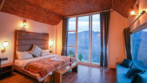 A bedroom with a large bed, a bench, a sofa, and a view of the mountains. - Dhara Doorway to Inner Peace (Kosiyakutoli)
