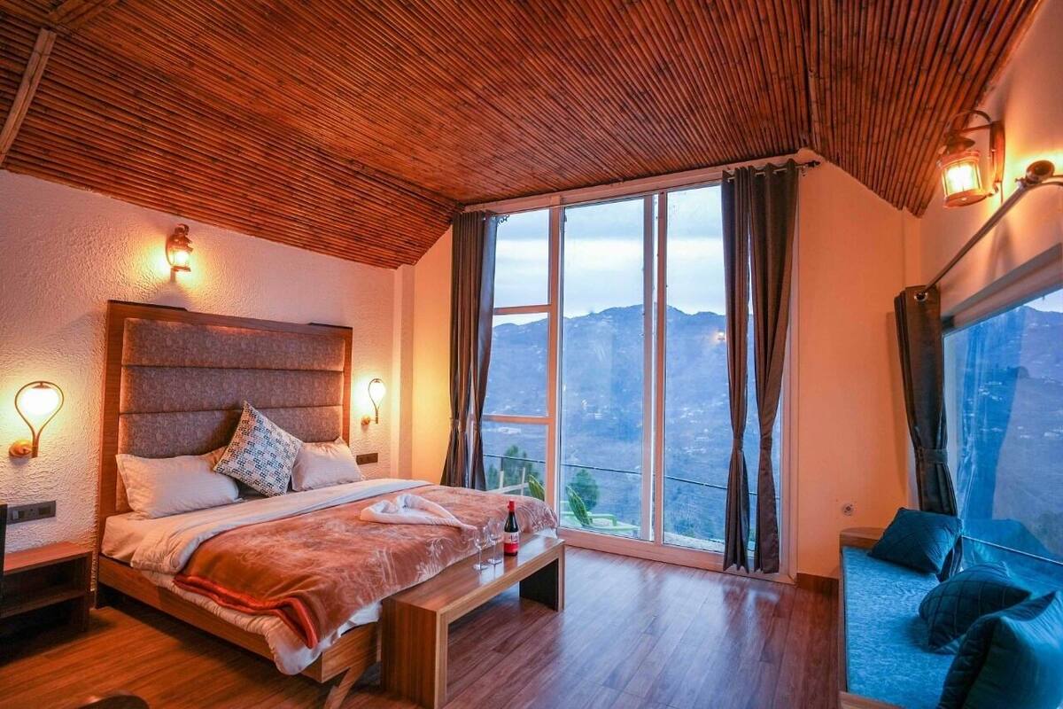 A bedroom with a large bed, a bench, a sofa, and a view of the mountains.
