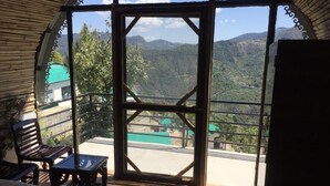 A room with a bed, a wooden bench, and a table. It has a large window with a view of a mountainous landscape. - Dhara Doorway to Inner Peace (Kosiyakutoli)