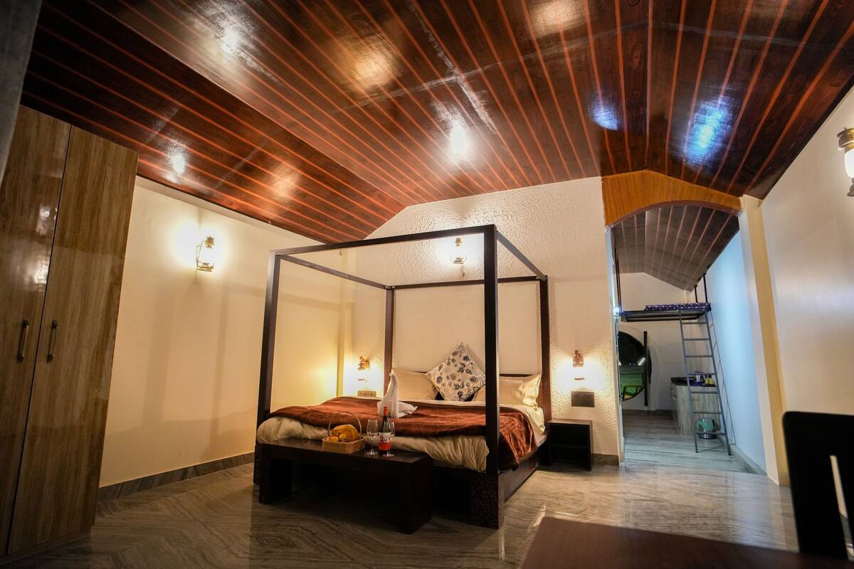 A four-poster bed with a wooden canopy, a bedside table with a lamp, and a small bedside table with a decorative item.