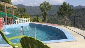A pool with a view of mountains, surrounded by greenery and a white fence. - Dhara Doorway to Inner Peace (Kosiyakutoli)