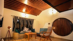 A cozy living room with a wooden ceiling, a round wooden door, and a seating area with a sofa and a chair. - Dhara Doorway to Inner Peace (Kosiyakutoli)