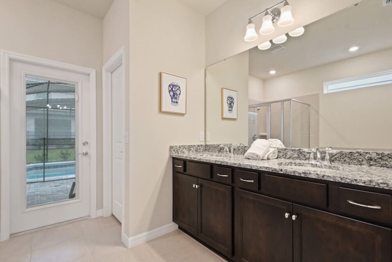 A bathroom with a large mirror, dark wooden cabinets, a granite countertop, and a shower area.