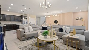 Een moderne woonkamer met een grijze hoekbank, een ronde salontafel en een keuken op de achtergrond.