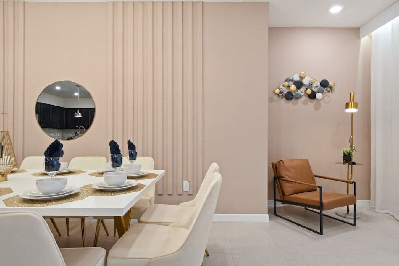 A dining area with a white table set for four, a round mirror, a modern chair, and a decorative wall piece.