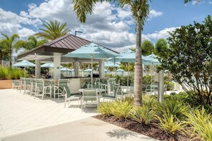 An outdoor patio area with tables and chairs, umbrellas, and a bar area.
