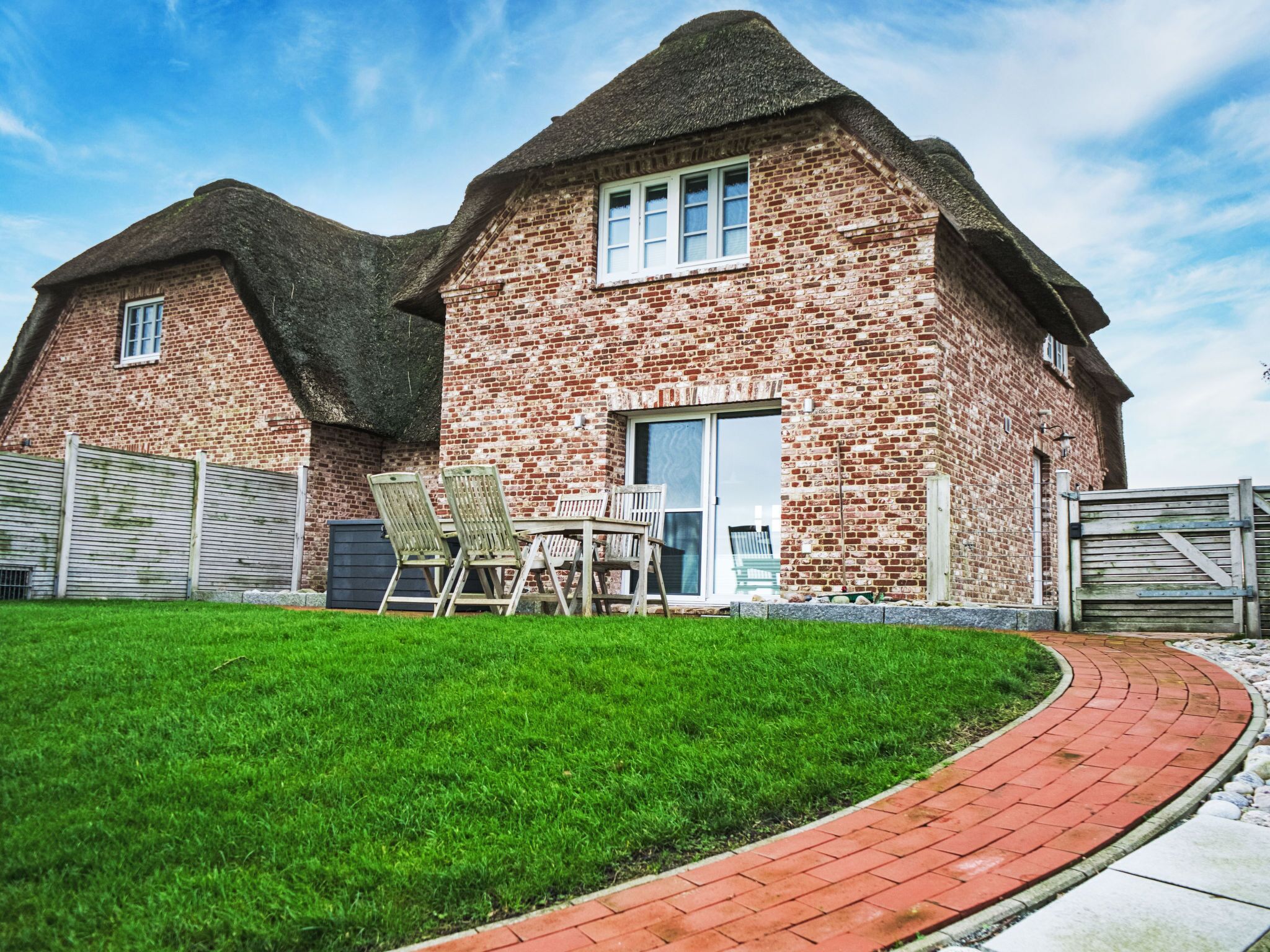 A brick house with a thatched roof, a paved driveway, and a well-maintained lawn.