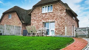 A brick house with a thatched roof, a paved driveway, and a well-maintained lawn.