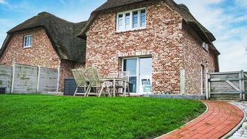 A brick house with a thatched roof, a paved driveway, and a well-maintained lawn.