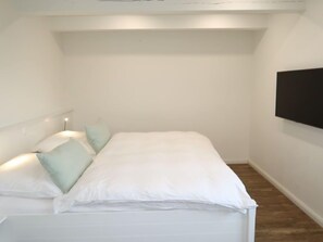 A small, white, single-bed room with a wooden floor, a flat-screen TV mounted on the wall, and a bedside table with a lamp. - Steuerbord by Interhome (Dagebüll)