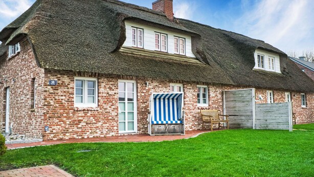 A traditional brick house with a thatched roof, a number '16' sign, and a blue-striped awning.