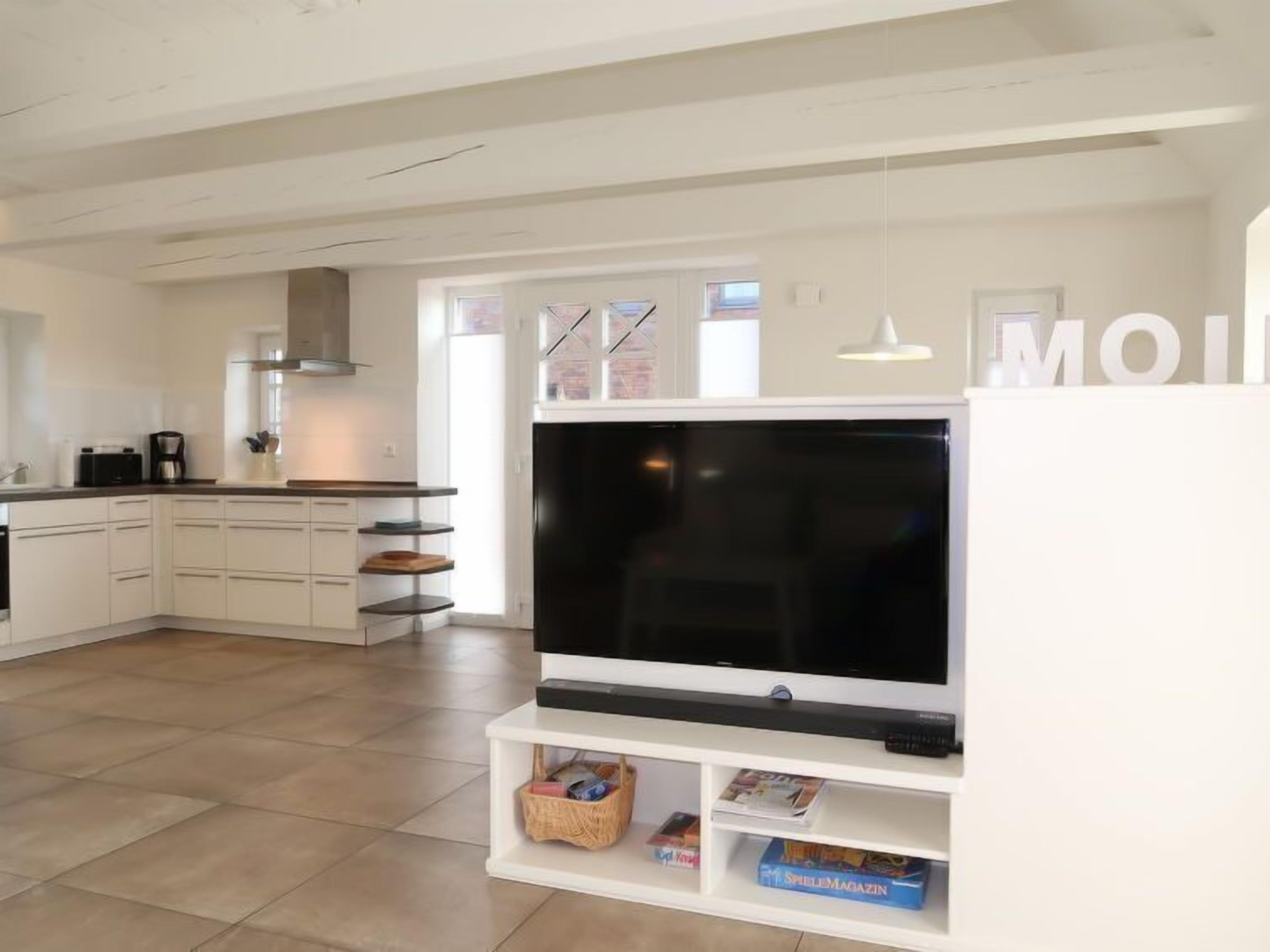 A modern kitchen with white cabinetry, a large flat-screen TV, and a dining area with a white table and chairs.