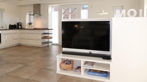 A modern kitchen with white cabinetry, a large flat-screen TV, and a dining area with a white table and chairs.