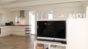 A modern kitchen with white cabinetry, a large flat-screen TV, and a dining area with a white table and chairs.