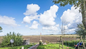 A pathway leading to a rural landscape with a field, a flagpole, and a swing set.