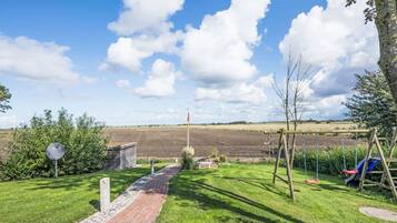 A pathway leading to a rural landscape with a field, a flagpole, and a swing set.