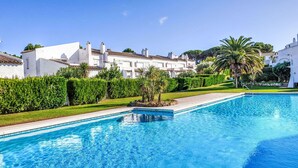 Una piscina amb superfície d'aigua blava i cristal·lina, envoltada de bous perfectament tallats i una palmera. Al fons, hi ha edificis blancs amb teules vermelles.
