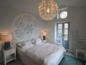 Une chambre avec un grand lit, deux tables de chevet, un élément de décoration circulaire fixé au mur, un luminaire suspendu, une fenêtre avec vue et une chaise blanche.