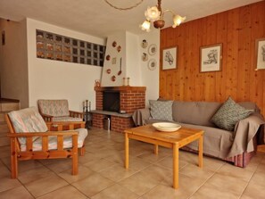A cozy living room with a fireplace, wooden walls, a sofa, a chair, and a table.