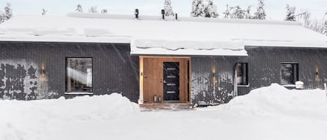 A modern building with a wooden door and windows, surrounded by snow.