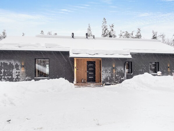 A modern building with a wooden door and windows, surrounded by snow.