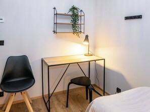 A small, neatly arranged room with a desk, two chairs, a bedside table, and a wall-mounted shelf with a plant. - Vaaranhelmi by Interhome (Kuusamo)