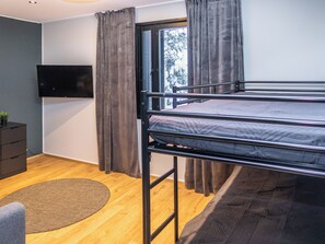 A compact room with a bunk bed, a television, a desk, and a window with curtains.