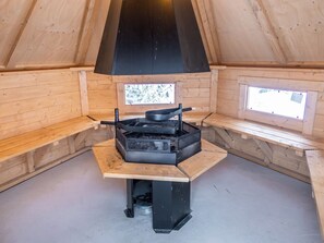 A wooden interior with a black stove, windows, and a bench.