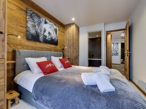 Slaapkamer met een groot bed, houten wanden, een opgehangen berenbeeld en een zichtbare badkamer.