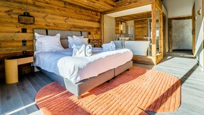 Une chambre à coucher de style cabane en bois, avec un grand lit, des tables de chevet et une salle de bain visible à travers une porte ouverte.