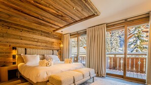 Une chambre avec un plafond en bois, un grand lit avec des oreillers, une table de chevet et une vue sur un paysage enneigé par une porte vitrée.