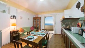 A dining area with a wooden table set for four, a cabinet with glass doors, and a view through a doorway to the outside. - Raphael House, terrace with solarium and sea view (Conca dei Marini)