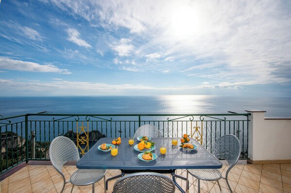 A balcony with a table set for breakfast, overlooking the sea.