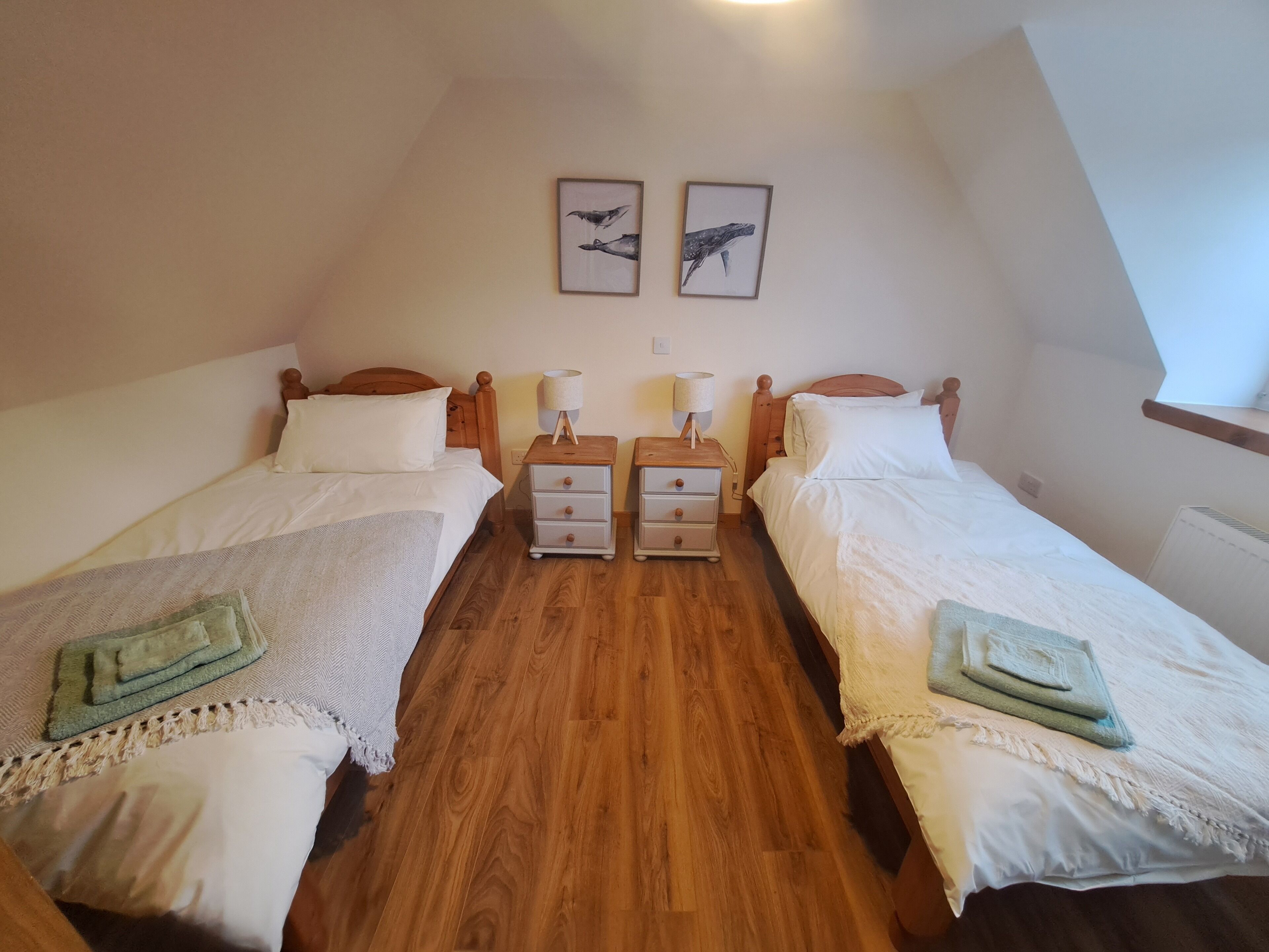 Une chambre avec deux lits simples, des têtes de lit en bois, une table de chevet avec une lampe et une étagère fixée au mur.