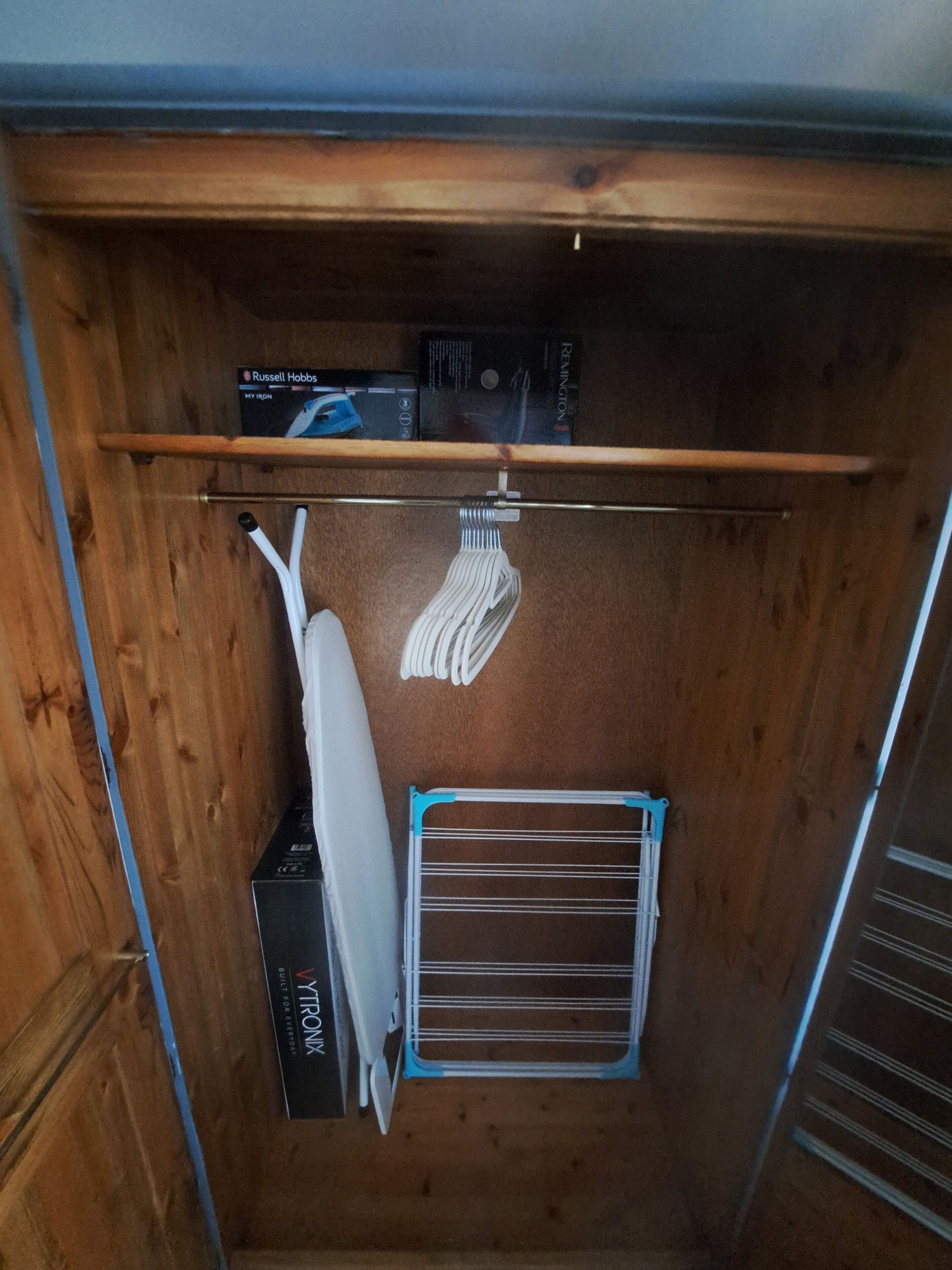 A wooden closet with a hanging rack, a drying rack, and boxes labeled "Russell Hobbs" and "VIRONA".