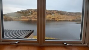Näkymä ikkunasta, jossa näkyy järvi ja taustalla kumpuilevia kukkuloita.