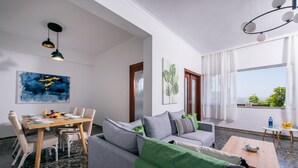A modern living room with a grey sofa, a dining table with chairs, and a balcony with a view. - Sunset View Apartment (Chania)