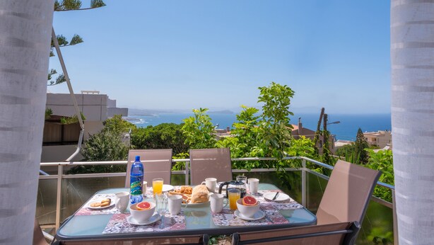 A balcony table with breakfast items and a view of the sea. - Sunset View Apartment (Chania)