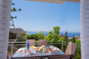 Mesa en el balcón con alimentos para el desayuno y vista al mar.