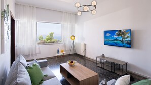 A modern living room with a sofa, coffee table, and a painting of a tropical beach. - Sunset View Apartment (Chania)