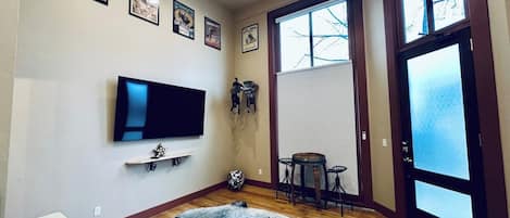 Una sala de estar con una televisión de pantalla plana, una alfombra, una mesita y una puerta con paneles de vidrio esmerilado.