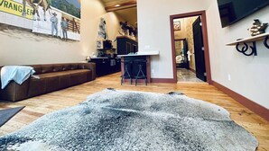 Ein geräumiges Wohnzimmer mit großem Teppich, einer Couch, einer Küchenzeile und einem Wand-Fernseher.