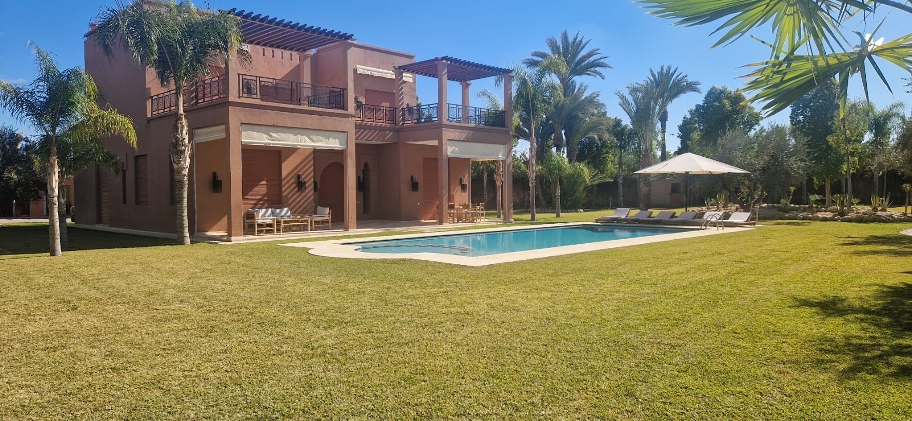 A two-story building with a swimming pool, surrounded by palm trees and a well-maintained lawn.