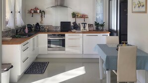 Une cuisine moderne avec des armoires blanches, un four encastré et un coin repas agrémenté d’une nappe à motifs.