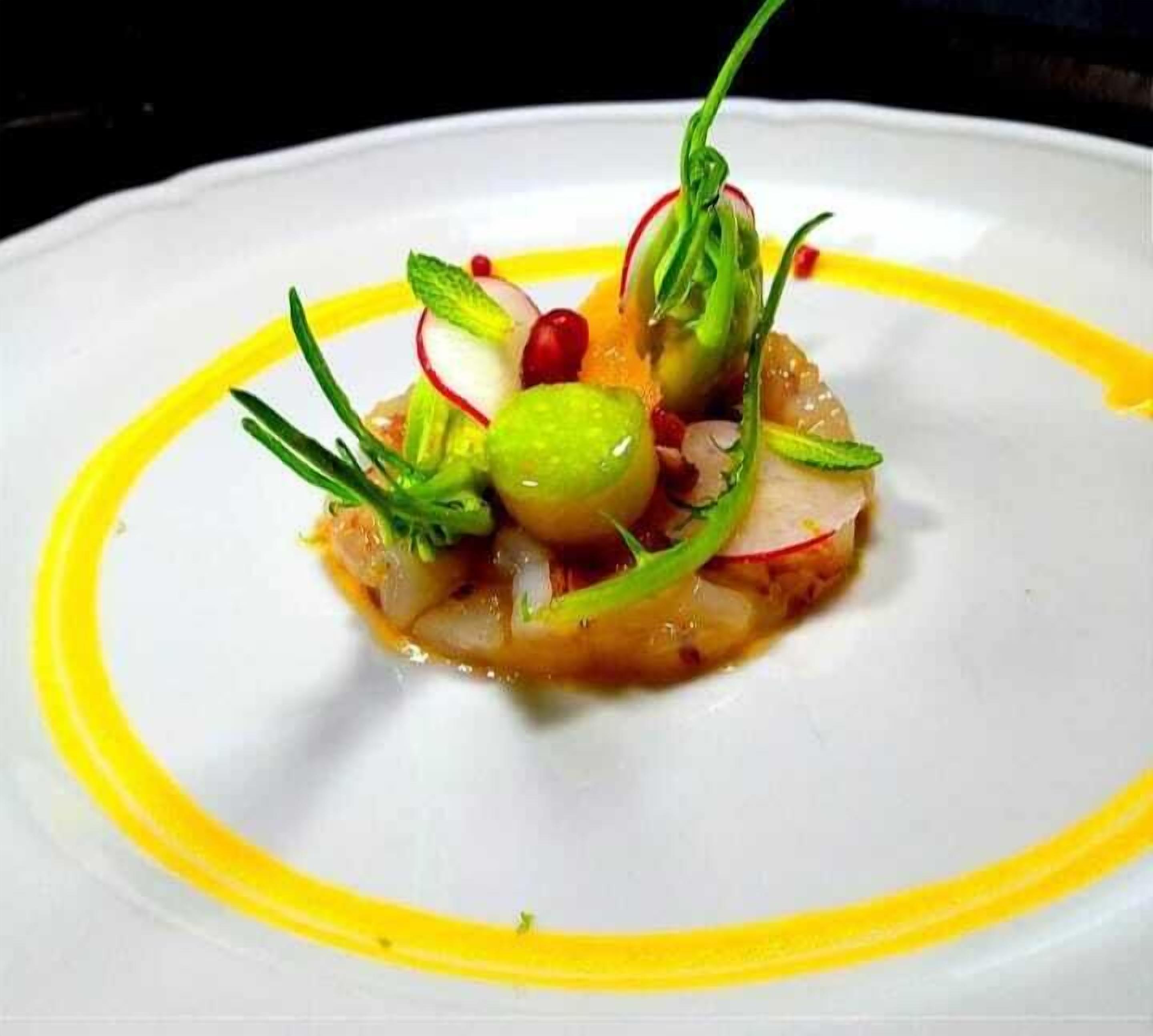 A white plate with a yellow rim, containing a dish with green vegetables, red berries, and a sauce.