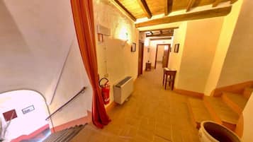 A narrow hallway with a tiled floor, a fire extinguisher, a radiator, and a staircase leading to another room.